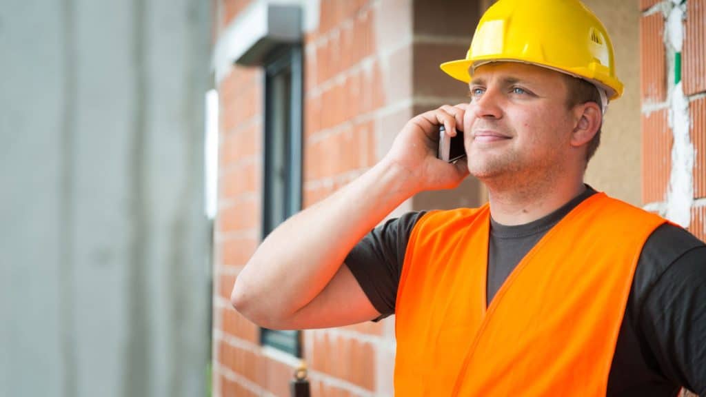 Construction worker in hard hat and safety vest on a phone call at a job site